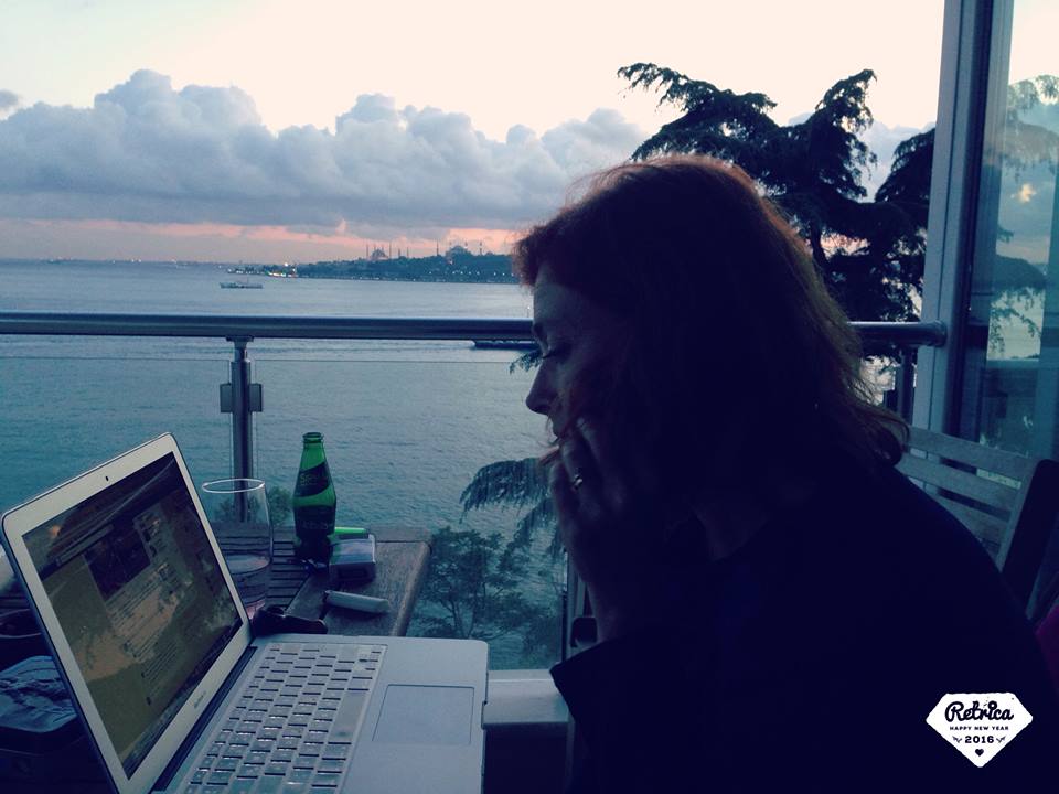 Wendy Wiseman turned in profile sitting at desk with ocean and sunset in background