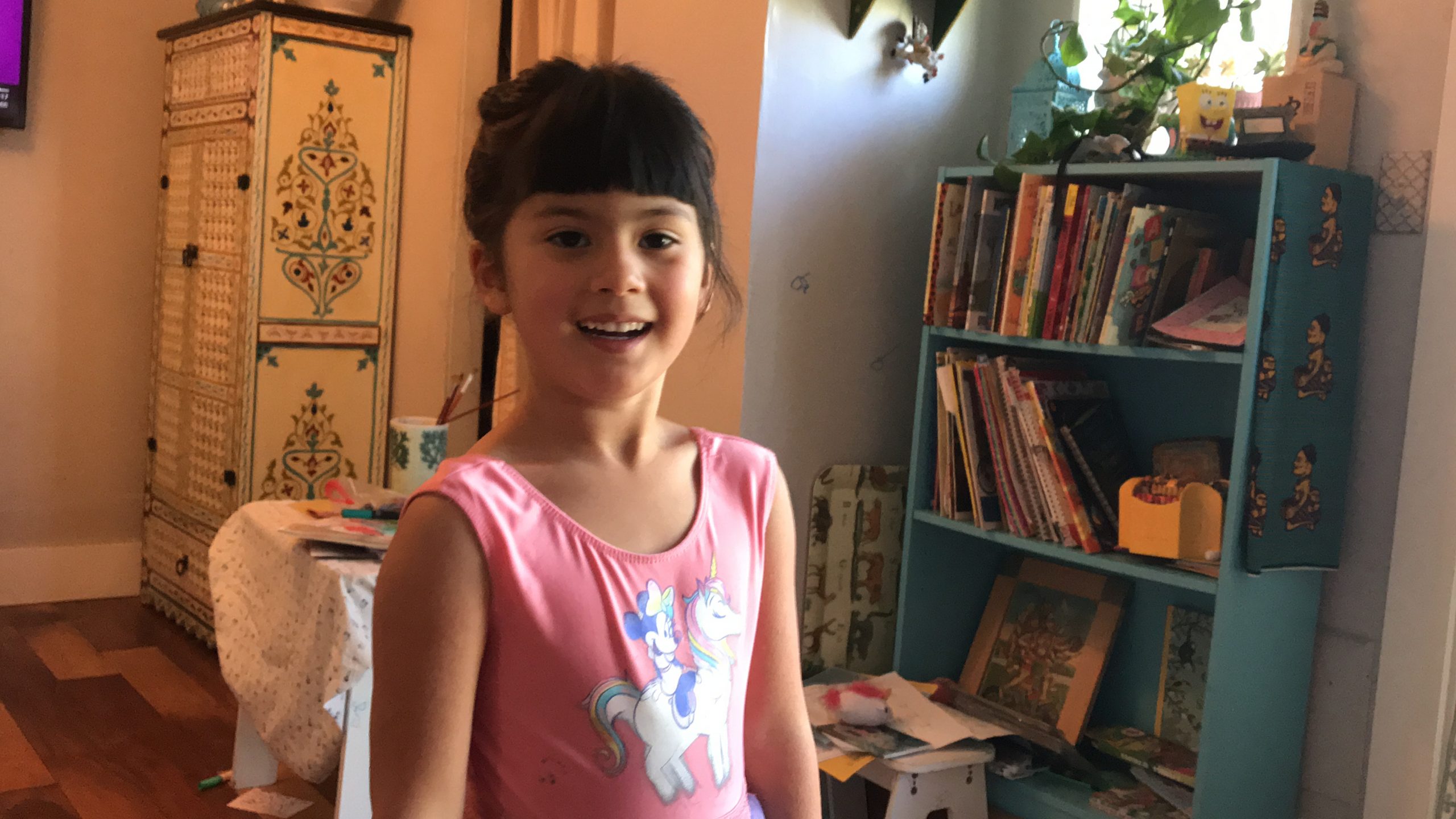 A girl in a pink shirt in front of a bookshelf