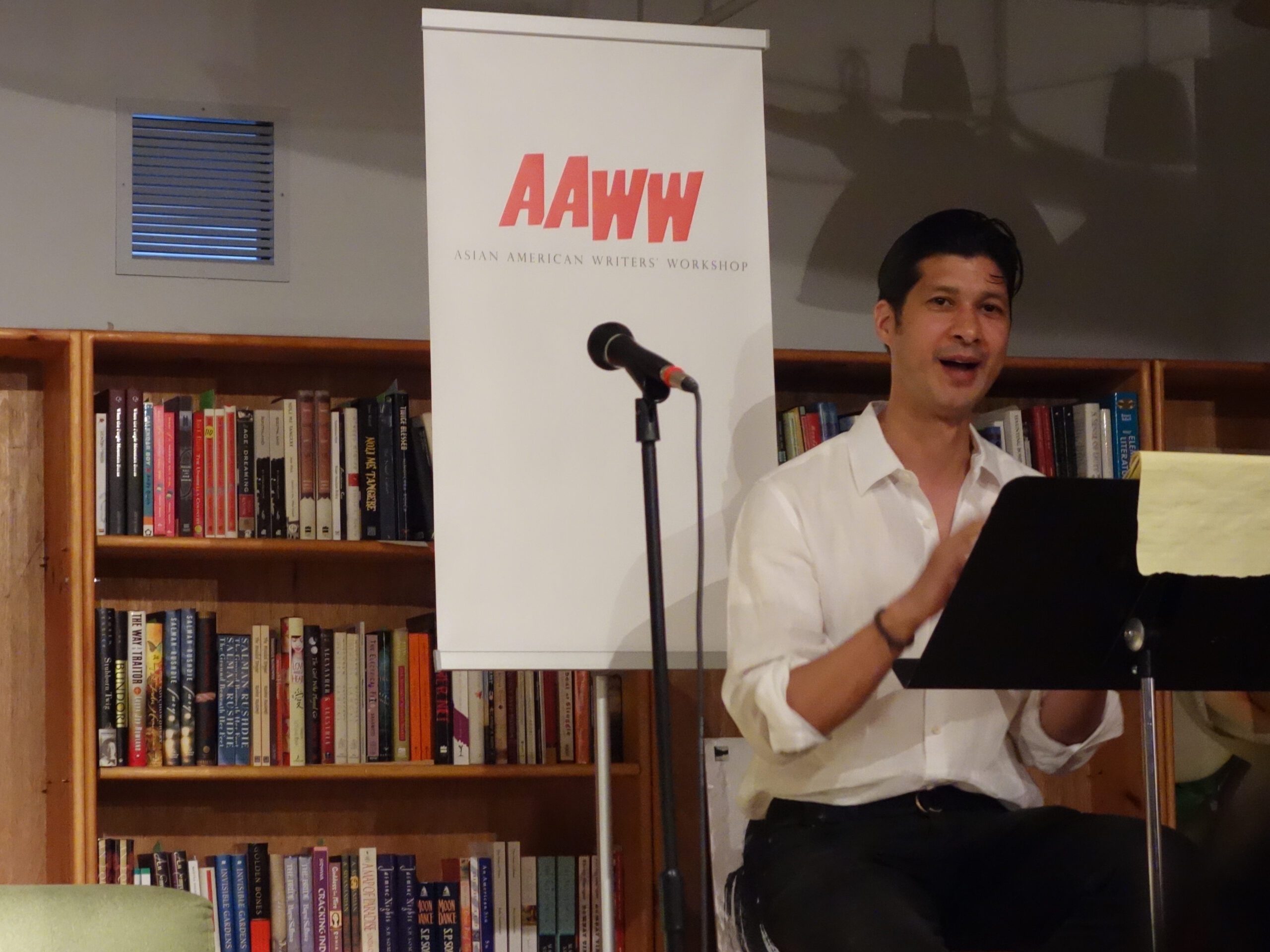 William Elison speaking at AAWW (Asian American Writers' Workshop) in front of a bookshelf