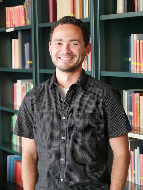 aj headshot in front of bookcase filled with books